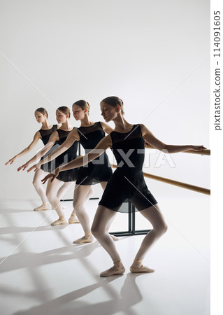 Ballet artistry. Beautiful talented teen girls, ballet dancers in black costumes standing at barre and practicing with focus and determination 114091605