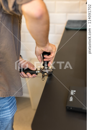 Barista leveling ground coffee in a portafilter with a tamper Barista leveling ground coffee in a portafilter with a tamper 114091702