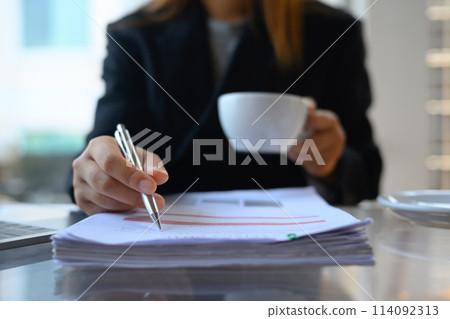 Cropped shot businesswoman working with document and drinking coffee at her workplace 114092313