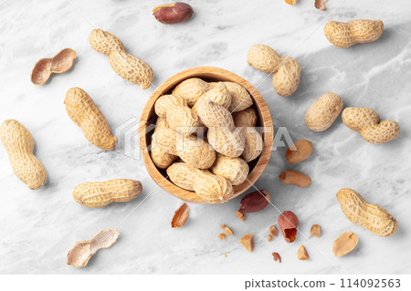 Roasted peanuts with shell in wood bowl on white marble table, top view 114092563