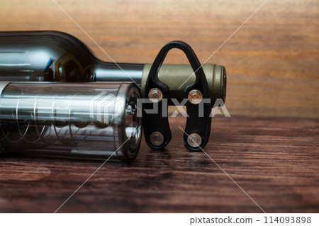 An electric corkscrew, a bottle of wine and a bottle opener lie on a dark wood background An electric corkscrew, a bottle of wine and a bottle opener lie on a dark wood background 114093898