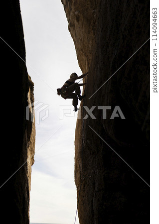 A person is climbing a rock wall in a cave A person is climbing a rock wall in a cave 114094663