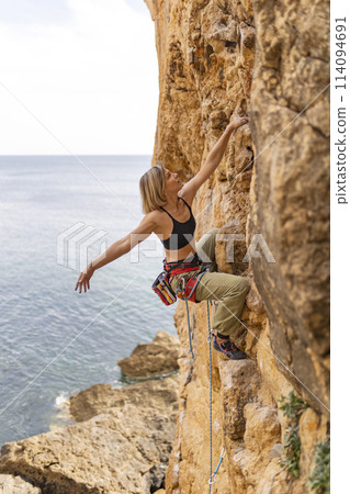 A woman is climbing a rock wall with a rope 114094691