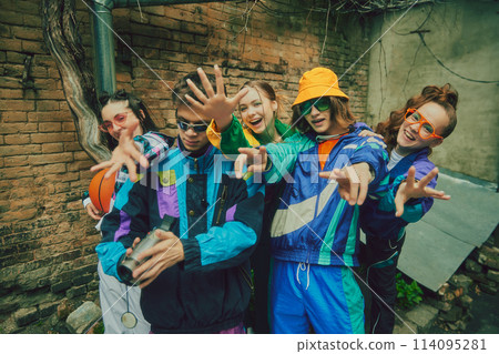 Vintage aesthetic fashion. Young people, friends wearing colorful athletic sportswear, trendy accessories posing in striking pose against urban backdrop 114095281