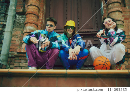 Friends meeting outdoors, boys and girl wearing stylish vivid sportswear, sunglasses and comfortable sport shoes, posing against vintage door background 114095285