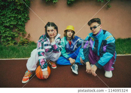 Retro street style. 90s inspired fashion. Young people, friends wearing colorful tracksuits, sunglasses, shoes and accessories, sitting outdoor Retro street style. 90s inspired fashion. Young people, friends wearing colorful tracksuits, sunglasses, shoes and accessories, sitting outdoor 114095324