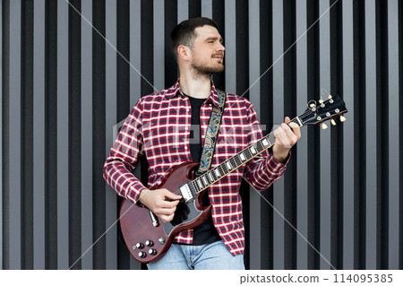 A stylish young guy plays the guitar on a dark background 114095385