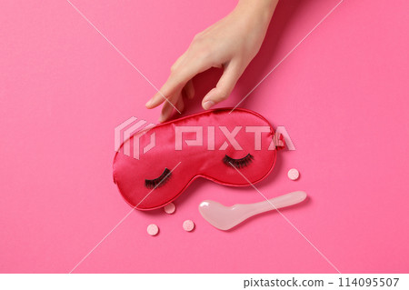 Sleep mask, pills, facial massager and hand on pink background, top view 114095507