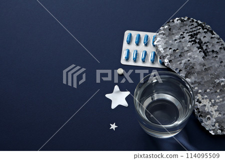Sleep mask, pills and glass on blue background, space for text 114095509