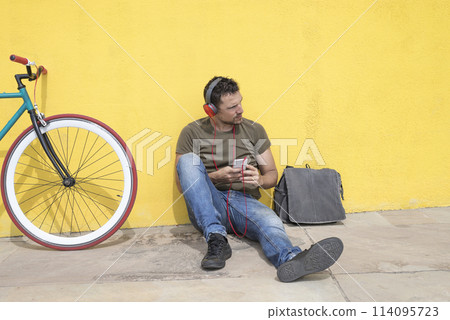 Man with headphones sitting by bike Man with headphones sitting by bike 114095723