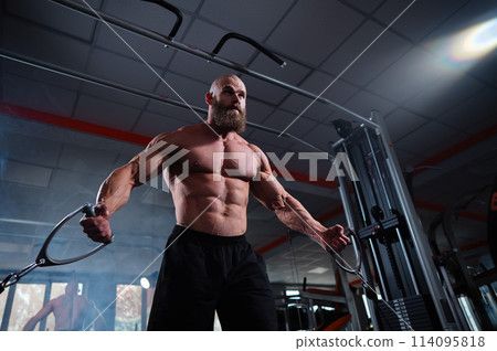 Bald Caucasian bodybuilder training chest using cable crossover in gym. Bald Caucasian bodybuilder training chest using cable crossover in gym. 114095818
