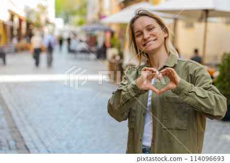 Woman makes symbol of love, showing heart sign to camera, express romantic feelings on city street 114096693