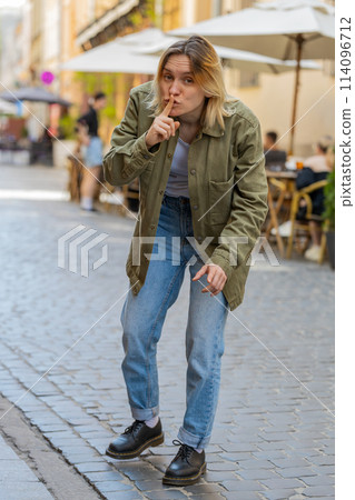 Young woman makes silence hush gesture sign asking do not tells gossip secret on urban city street Young woman makes silence hush gesture sign asking do not tells gossip secret on urban city street 114096712