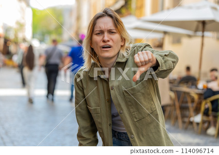 Upset young woman showing thumbs down sign disapproval, dissatisfied bad feedback on city street Upset young woman showing thumbs down sign disapproval, dissatisfied bad feedback on city street 114096714