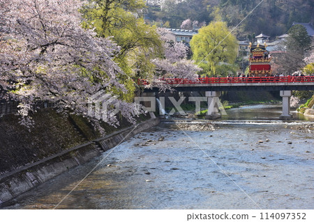 Takayama City, Gifu Prefecture, Japan, Spring Takayama Festival, Cherry blossoms in full bloom and food stalls crossing Nakabashi Bridge, beautiful fresh greenery and blue sky 114097352