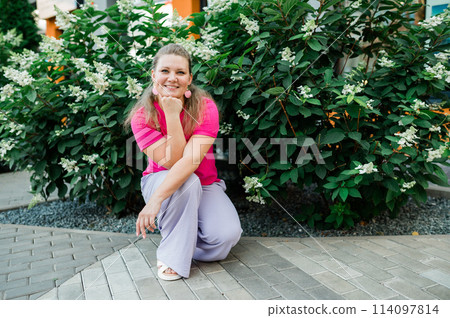 Portrait of beautiful smiling millennial woman wearing stylish pink t shirt looking at camera standing in green park. Positive lifestyle, natural beauty concept. Copy space 114097814