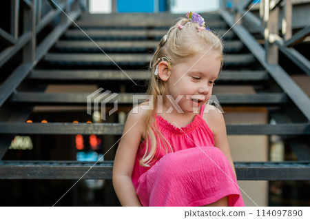 Child girl with hearing aids and cochlear implants having fun outdoor speak and playing. Inclusion and disability. 114097890