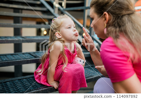 Deaf child with cochlear implant for hearing audio and aid for impairment having fun and laughs with mother outdoor in summer. Sound fitting device to help with communication listening and interaction 114097892