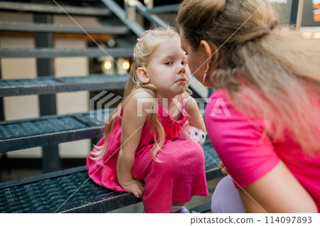 Deaf child with cochlear implant for hearing audio and aid for impairment having fun and laughs with mother outdoor in summer. Sound fitting device to help with communication listening and interaction 114097893
