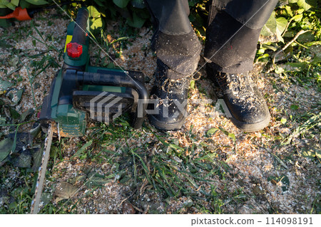 Close up of electric saw and boots on sawdust. Close up of electric saw and boots on sawdust. 114098191