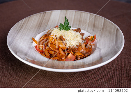 Beef stew with pasta and tomatoes on a plate with cheese topping 114098302