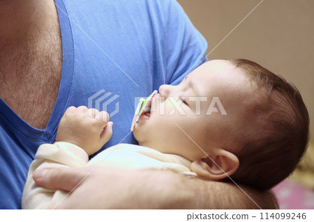 Cute newborn baby sleeping in father arms close up. A loving father carries her newborn baby at home. portrait of a happy mother holding a sleeping baby Cute newborn baby sleeping in father arms close up. A loving father carries her newborn baby at home. portrait of a happy mother holding a sleeping baby 114099246