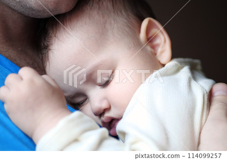 Cute newborn baby sleeping in father arms close up. A loving father carries her newborn baby at home. portrait of a happy mother holding a sleeping baby Cute newborn baby sleeping in father arms close up. A loving father carries her newborn baby at home. portrait of a happy mother holding a sleeping baby 114099257