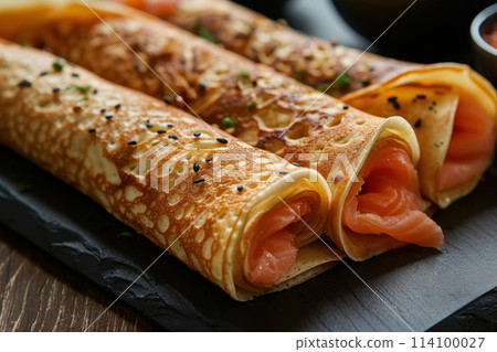 Three homemade thin pancakes stuffed with salmon, close up black plate, rustic style on wooden background Three homemade thin pancakes stuffed with salmon, close up black plate, rustic style on wooden background 114100027