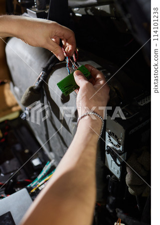 Auto electrician is connecting a wiring to car amplifier close up. 114101238