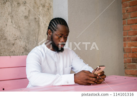Millennial generation african american man typing sms outdoor 5g internet concept. High speed internet on phone and chatting on social networks and blog concept 114101316