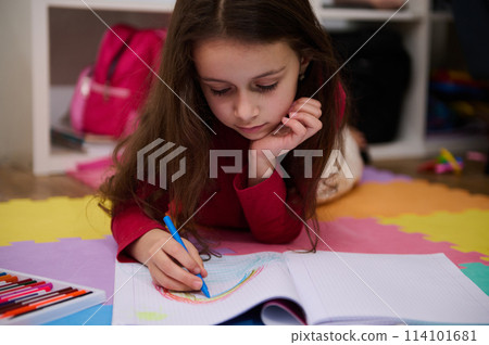 Adorable little child girl drawing rainbow with pastel pencils, lying on a multicolored puzzle carpet in her room at home. Art and creativity concept. Kids development, education. Hobbies and leisure Adorable little child girl drawing rainbow with pastel pencils, lying on a multicolored puzzle carpet in her room at home. Art and creativity concept. Kids development, education. Hobbies and leisure 114101681