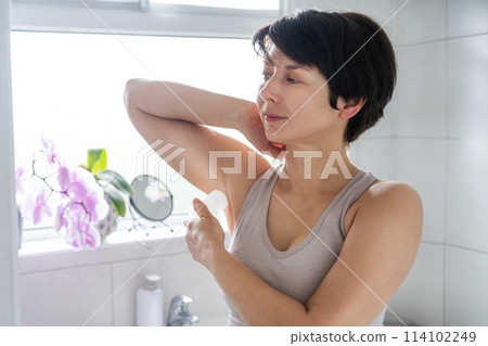 Young woman applying natural crystal alum deodorant in light modern bathroom. Eco friendly natural beauty and hygiene cosmetics. Zero waste, sustainable, alternative body care concept. Selective focus Young woman applying natural crystal alum deodorant in light modern bathroom. Eco friendly natural beauty and hygiene cosmetics. Zero waste, sustainable, alternative body care concept. Selective focus 114102249