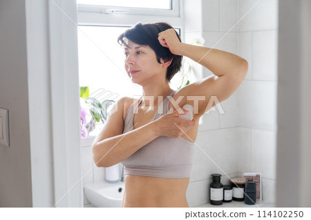 Young woman applying natural crystal alum deodorant in light modern bathroom. Ecofriendly natural beauty and hygiene cosmetics. Zero waste, sustainable, alternative body care concept. Selective focus. Young woman applying natural crystal alum deodorant in light modern bathroom. Ecofriendly natural beauty and hygiene cosmetics. Zero waste, sustainable, alternative body care concept. Selective focus. 114102250