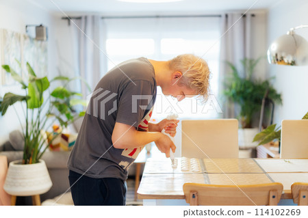 Concentrated young man placing batter on silicone baking sheet to make French macaroons dessert in light modern kitchen at home. Preparing steps for baking cookies. Culinary hobby. Selective focus Concentrated young man placing batter on silicone baking sheet to make French macaroons dessert in light modern kitchen at home. Preparing steps for baking cookies. Culinary hobby. Selective focus 114102269