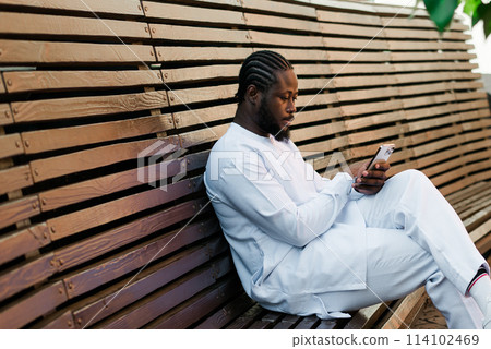 Millennial generation african american man typing sms outdoor 5g internet concept. High speed internet on phone and chatting on social networks and blog concept Millennial generation african american man typing sms outdoor 5g internet concept. High speed internet on phone and chatting on social networks and blog concept 114102469