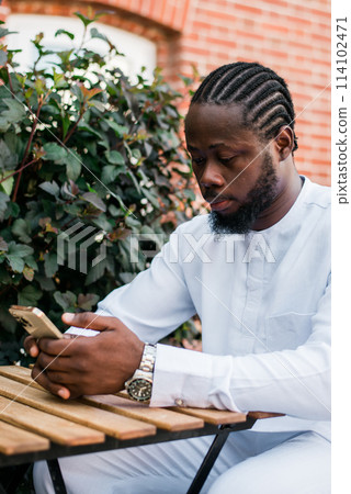 Millennial generation african american man typing sms outdoor 5g internet concept. High speed internet on phone and chatting on social networks and blog concept Millennial generation african american man typing sms outdoor 5g internet concept. High speed internet on phone and chatting on social networks and blog concept 114102471
