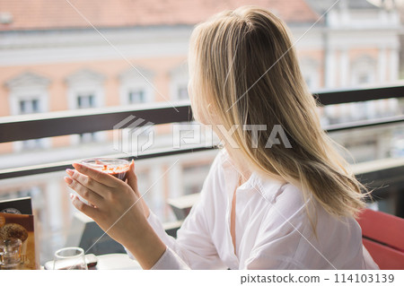 Gen z blonde woman drinks hot chocolate in summer cafe. Tasty beverage and break concept. Generation z people 114103139