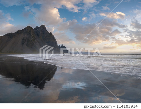Sunrise Stokksnes cape sea beach and Vestrahorn Mountain with its reflection on wet black volcanic sand surface, Iceland. Amazing nature scenery, popular travel destination. Sunrise Stokksnes cape sea beach and Vestrahorn Mountain with its reflection on wet black volcanic sand surface, Iceland. Amazing nature scenery, popular travel destination. 114103914