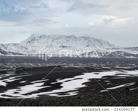 Autumn snowfall in Iceland highlands. Colorful Landmannalaugar mountains under snow cover in autumn, Iceland. Lava fields of volcanic sand in the foreground. 114104177