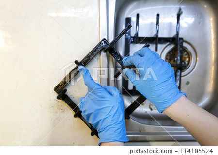 Cleaning the cast iron grill of the gas hob with a dishwashing wire. General cleaning concept, removing old grease stains, grease and old food residues. 114105524