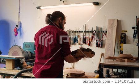 Carpenter selecting tool from rack to use on wood materials, helped by african american coworker. Craftsperson doing quality assurance on lumber pieces pile with BIPOC apprentice, camera A 114107122
