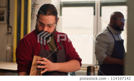 Manufacturer putting safety goggles on while selecting quality wood materials meeting client commission requirements. Woodworking expert doing quality assurance on timber block, camera A 114107142