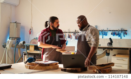 Carpenter and african american coworker verifying finished wood art product before sending it to client. Artisan and apprentice inspecting wooden object to correspond to requirements Carpenter and african american coworker verifying finished wood art product before sending it to client. Artisan and apprentice inspecting wooden object to correspond to requirements 114107148