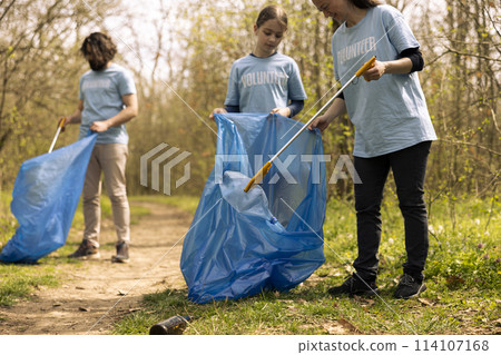 Diverse people collecting rubbish and storing in the trash disposal bag, picking up junk and plastic bottles to help with pollution. Clearing the forest, ecosystem protection. 114107168