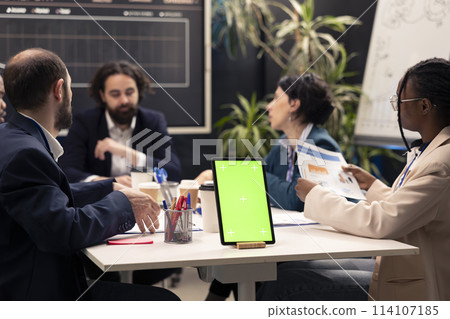 Chief executive officer hosts meeting with his staff next to mockup display, discussing latest business achievements and performance metrics. Workers share project updates or insight. 114107185