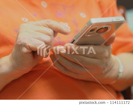 Hands of an elderly woman operating a smartphone Hands of an elderly woman operating a smartphone 114111172