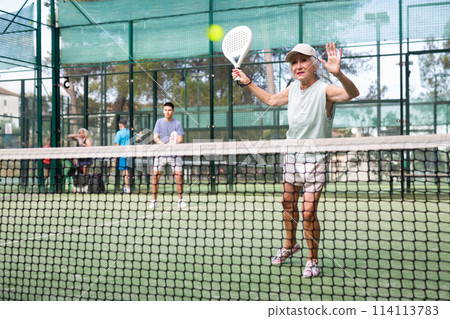 Senior woman playing padel tennis match during training on court Senior woman playing padel tennis match during training on court 114113783