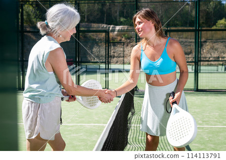Two women shake hands after playing padel on tennis court outdoor 114113791