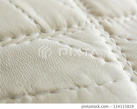 Close-up view of intricate stitching on a creamy leather surface, showcasing the material's luxurious quality. 114113828
