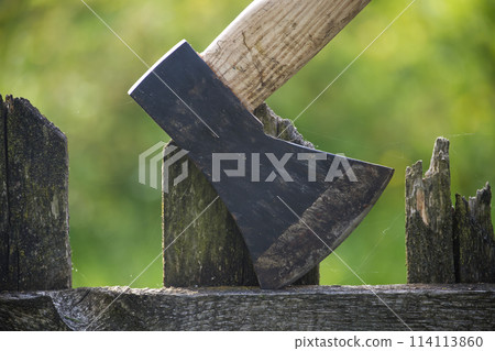 Detailed view of axe lodged into an old, weathered wooden fence 114113860